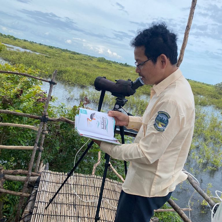 Tour guide on the Tonle Sap with a book, behind him a telescope